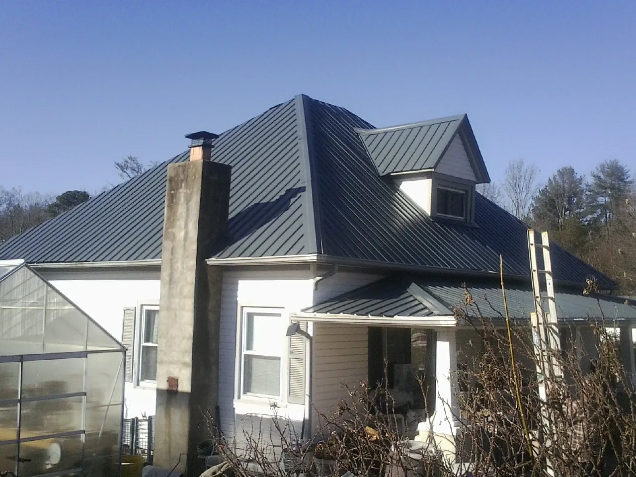 Dark blue standing seam metal roof on a white farmhouse with dormer — Slate & Tile Roof Repair by Roofing Brothers in New Kensington