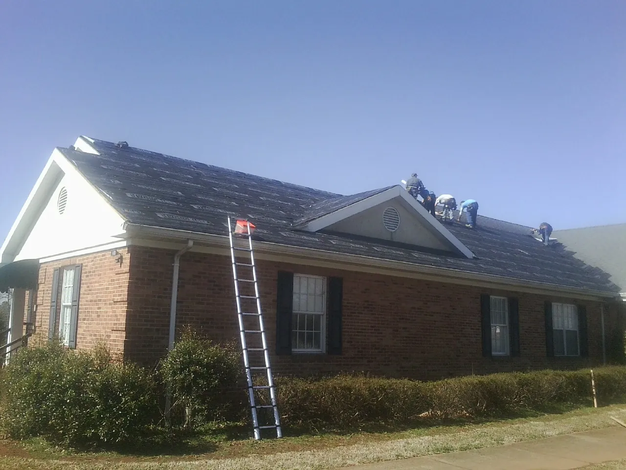 Crew tearing shingles off a brick ranch roof with a ladder set — Emergency Roof Repair work by our crew in New Kensington