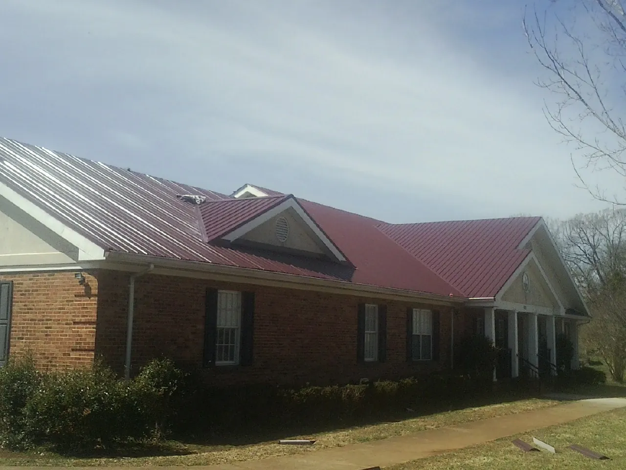 Red metal roof with gabled entries on a long brick building, from a Hail Damage Roof Repair job in New Kensington