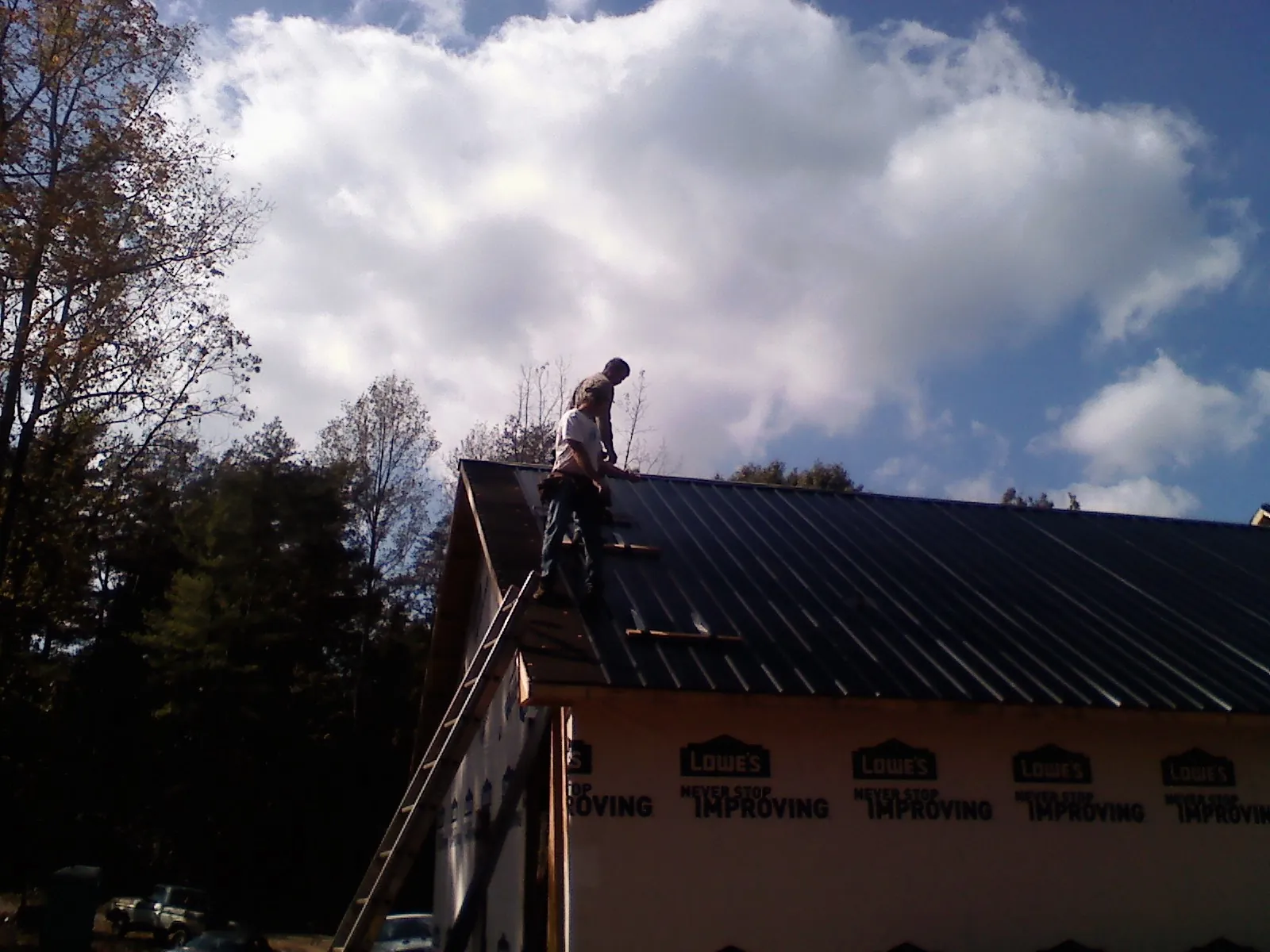 Roofer fastening dark metal panels high against a cloudy sky, from a Roof Inspection job in New Kensington