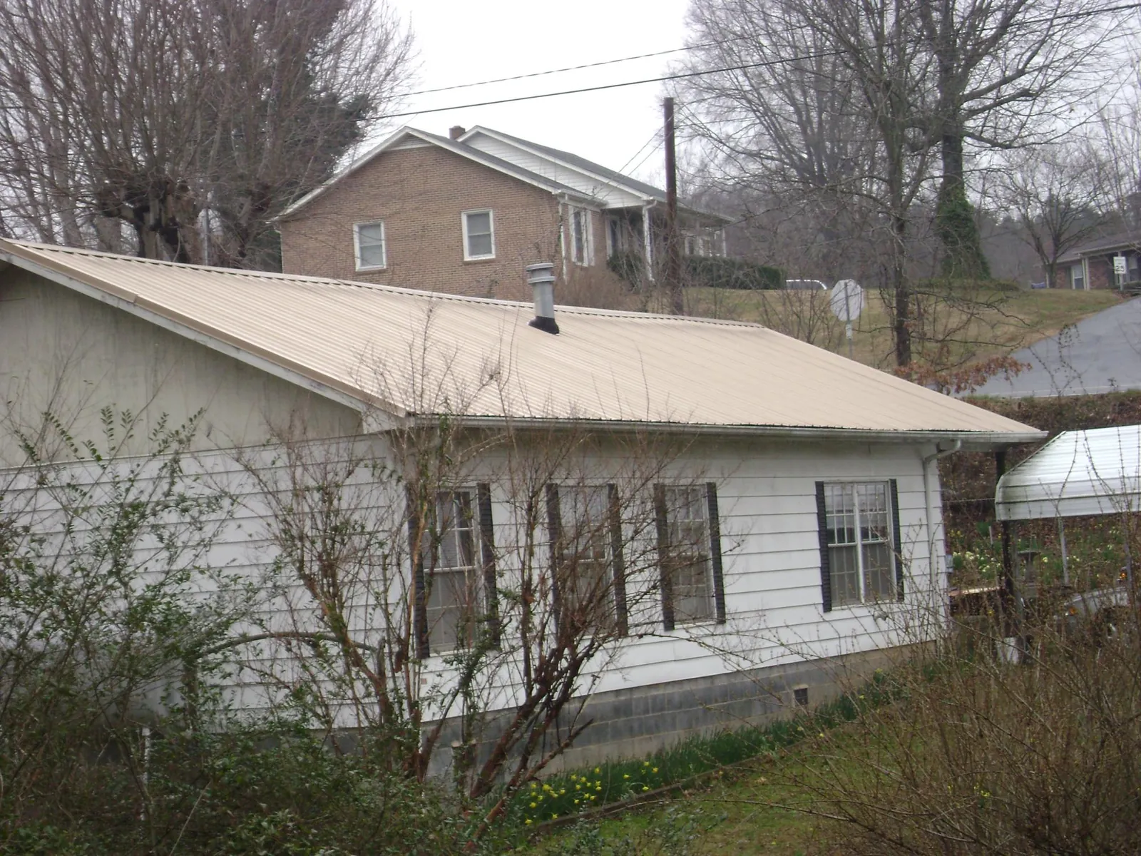 Tan metal roof on a white sided house set into a hillside — Commercial Roofing by Roofing Brothers in New Kensington